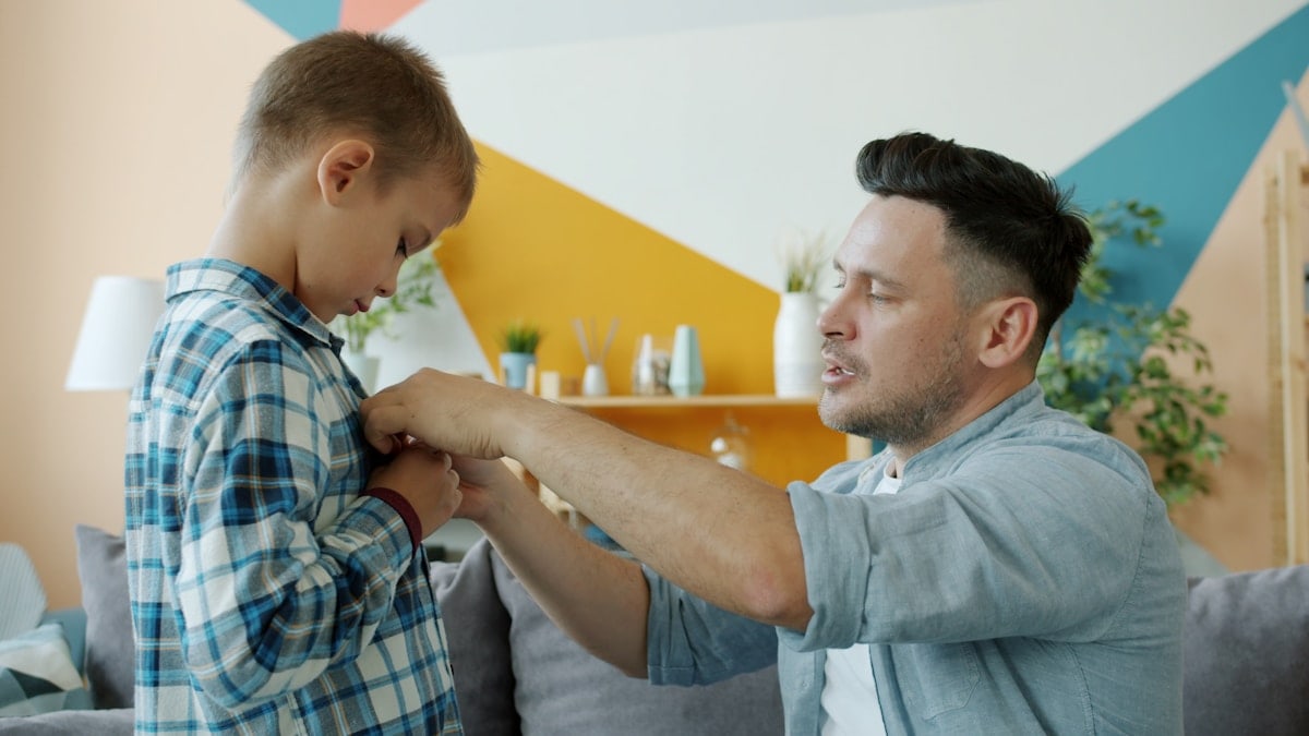 Loving dad middle-aged man is helping child with clothing talking then hugging expressing love at home. Family relationship and fatherhood concept.